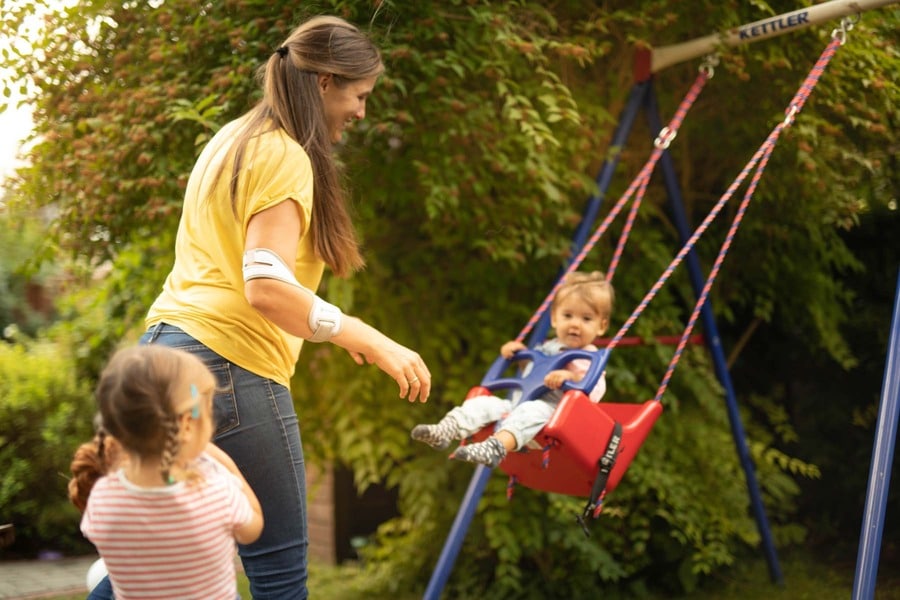 Frau schaukelt mit zwei Kindern und trägt dabei Masalo Manschette gegen Tennisarm, Golferarm, Mausarm