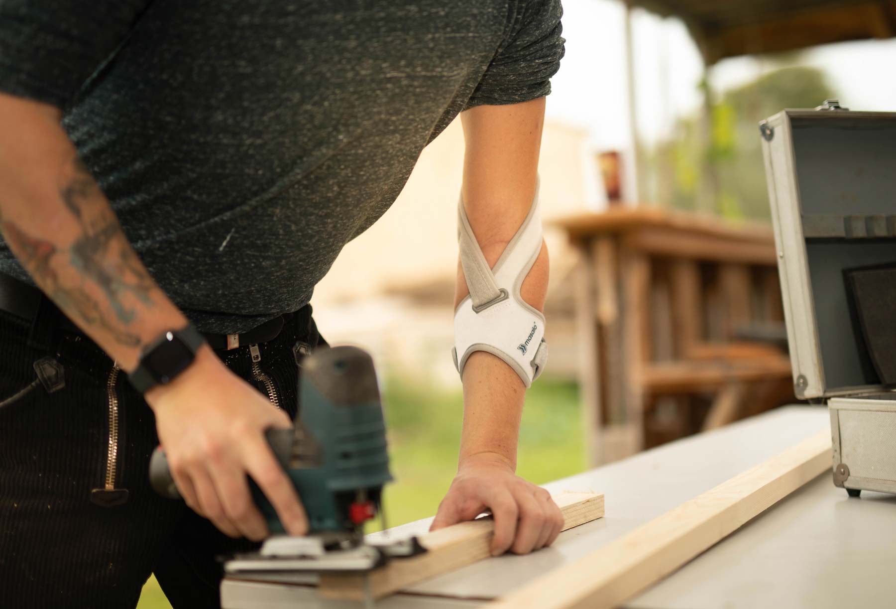 Mann mit Stichsäge arbeitet mit Masalo Manschette gegen Tennisarm, Golferarm, Mausarm