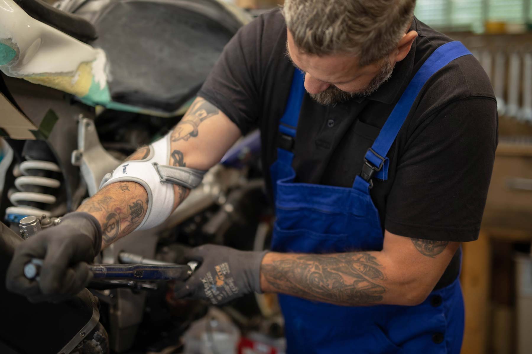 Mechaniker repariert Motorrad und trägt Blaumann und Masalo Manschette gegen Tennisarm