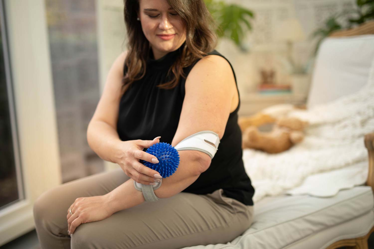 Woman wears Masalo cuff against tennis elbow and massages her elbow fascia with hedgehog ball