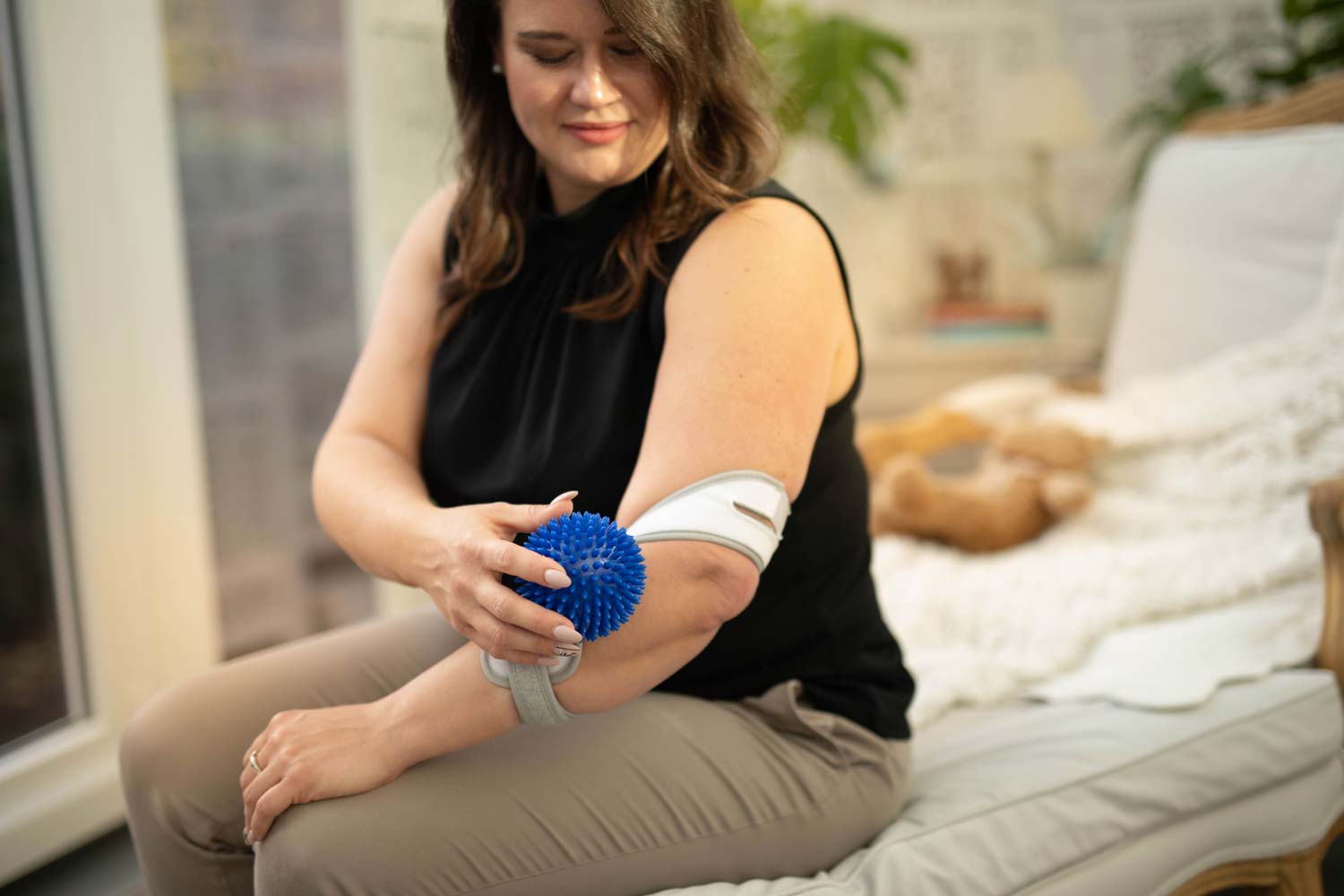 Masalo_Manschette_Igelball_Massage_bei_Epicondylitis_Tennisarm Frau trägt Masalo Manschette gegen Tennisarm und massiert sich mit Igelball die Faszien des Ellenbogens